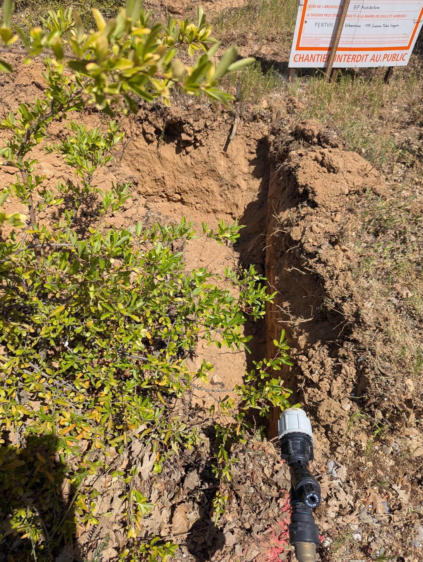Chantier de pose des canalisations d'irrigation dans le sol calcaire drainant provençal, avec raccord visible au fond de la tranchée, aux Jardins d'Hélios à Pertuis, juin 2026
